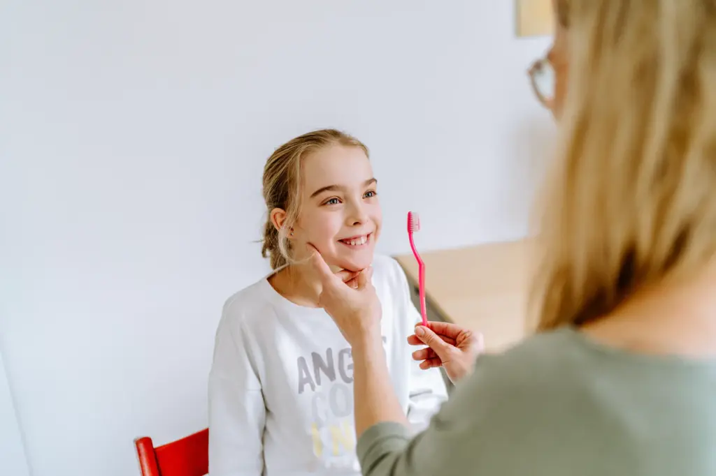 Logopädin mit Kind, sitzen sich gegenüber, machen eine logopädische Übung mit einer Zahnbürste