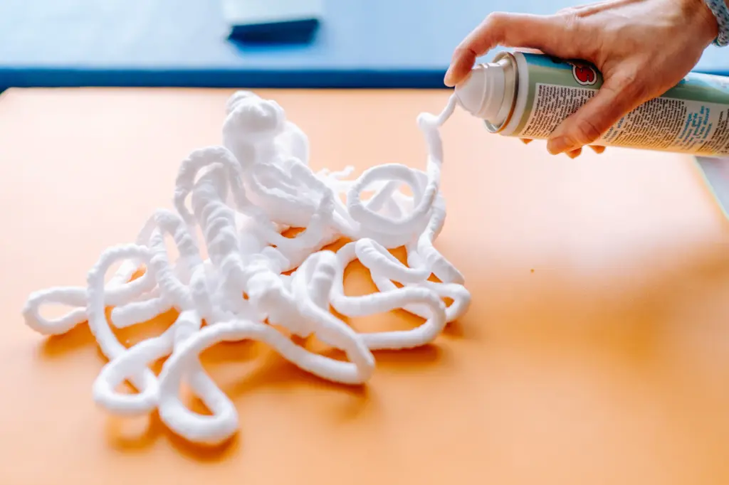 Hand mit Spieleschaum-Sprühflasche: Schaum wird auf eine Matte gesprüht.